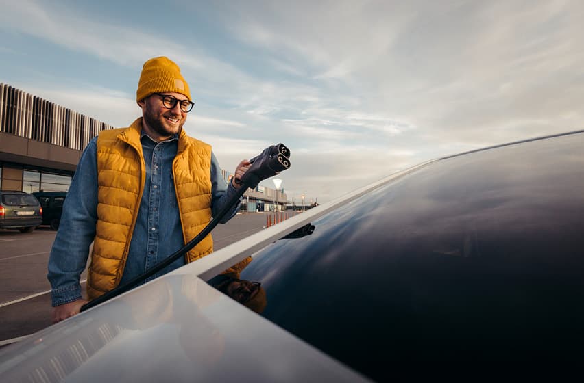 Man charging EV smiling wearing an orange beanie
